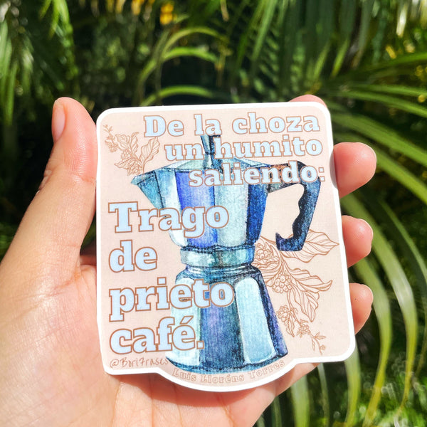 Sticker con las hojas de café, la famosa greca y la siguiente frase del poema "Café prieto" de Luis Lloréns Torres: "De la choza que está en la vereda, un humito saliendo se ve. La ventana se abre. Y la doña me da un trago de prieto café."